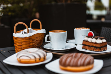 Slice of chocolate cake, Cutlery steak basket and donot with coffee on the table.