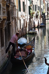 Fototapeta na wymiar Gondola driver with passengers pushing the gondola away from a building’s wall with his feet on an empty canal