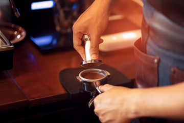 Barista holding portafilter and coffee tamper making  coffee at cafe.