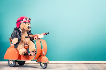 Selbstklebende Fototapeten Retro Teddy Bear toy in red helmet with goggles and leather jacket on old children's pedal orange scooter from 60s front mint blue wall background. Kid's race concept. Vintage style filtered photo © BrAt82