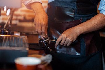 Barista holding portafilter and coffee tamper making  coffee at cafe.