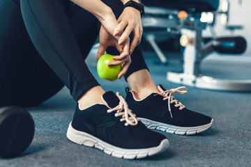 Naklejka premium Woman exercise workout in gym fitness break and relax. Hands holding apple fruit after training sport with dumbbell and water bottle beside her.