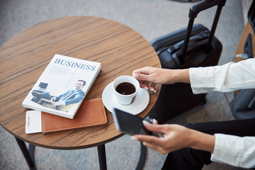 Young woman grabbing cup of coffee and using cellphone
