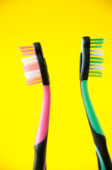 Two toothbrushes pink and green on a yellow background, oral hygiene