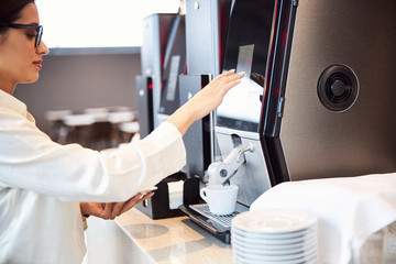 Beautiful young woman using automatic coffee machine