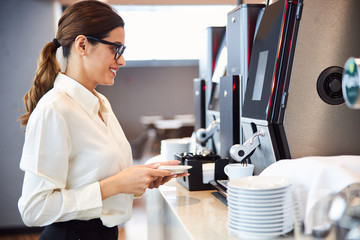 Smiling young woman using automatic coffee machine
