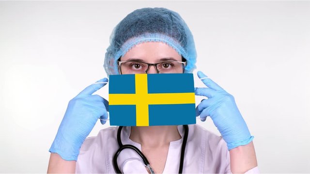 close-up. Doctor in glasses, blue medical cap, gloves holds in hands medical mask with Sweden flag. Physicians care, protection by state during coronavirus, global epidemic. Concept.