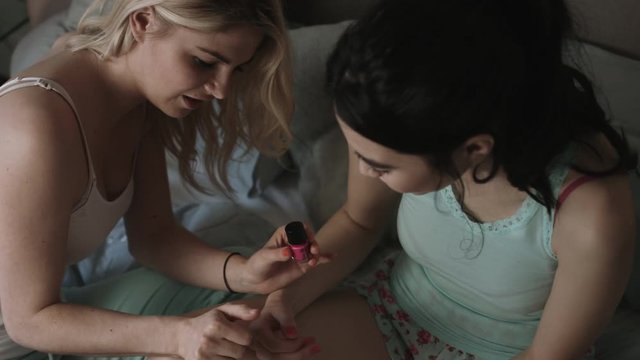 Young female friends applying nail polish in bedroom