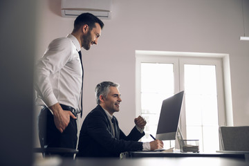 Happy male colleagues looking at screen of laptop
