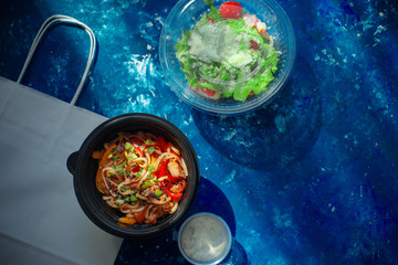 Take out flat lay with chicken udon and Ceasar salad in plastic packaging
