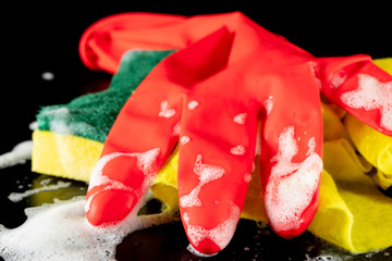 Scouring sponge foaming gloves and yellow cleaning cloth. In black background. Close up.