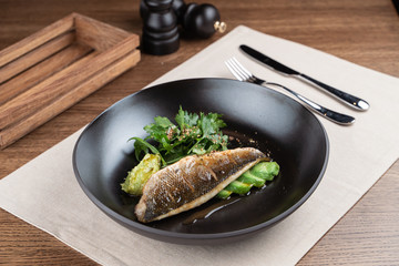 Roasted sea bass with parsley and avocado on a black plate