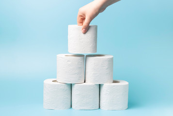 Female hand stacks toilet paper in a stack on blue background close-up.