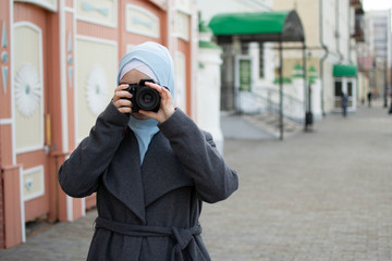 Muslim girl shoots a professional photographer in a blue shawl in a gray coat and pink dress