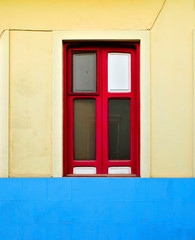 Fototapeta na wymiar One simple red window centered in a blue and yellow wall.