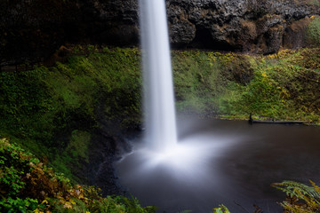 Long exposure of a waterfall at Silver Falls State Park, Silverton, Oregon, USA, in the Autumn, featuring yellow and green colors and a cave