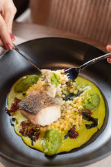 Woman is eating cod fillet baked with avocado puree and ptitim with knife and fork