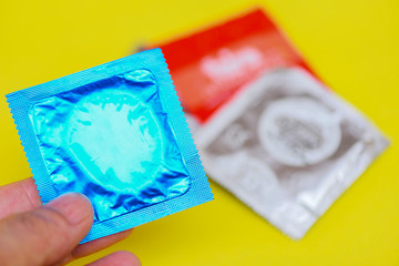 Condom in hand hold on yellow background - Colorful condom pack for birth control contraceptive...