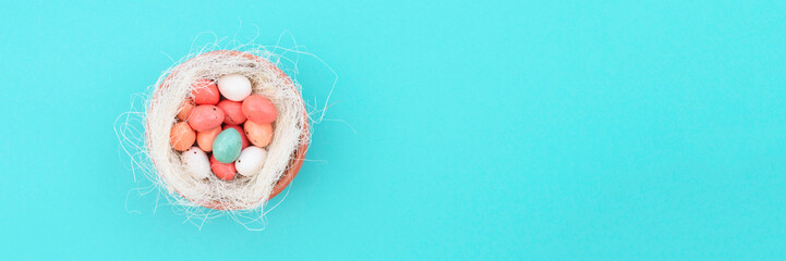 Decorative bird nest with colorful easter eggs on blue pastel background. Easter concept. Place for text. Banner.