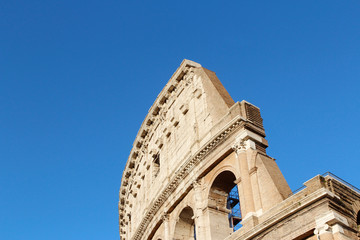The exterior facade of the Colosseum or Coliseum with the arches against blue clear sky in Rome,...