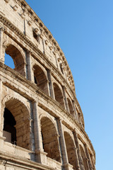 The exterior facade of the Colosseum or Coliseum with the arches against blue clear sky in Rome, Italy