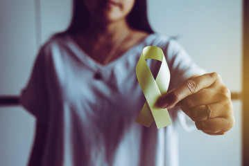 Woman hand holding yellow ribbon on color background,Suicide prevention,Cancer disease awareness...