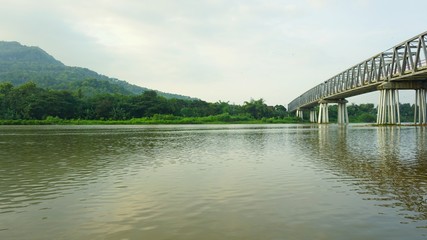 Fototapeta premium A view on the river bank and a long bridge over the river. Visible mountains across the river.