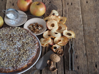 Round homemade fruit tart on a wooden ancient table with ingredients for sprinkling.Apple and plum chips are used. Place for text.