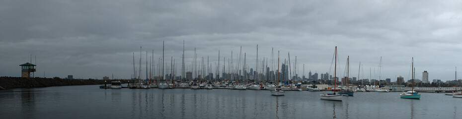 Fototapeta premium Panoramic of the city of Melbourne against a sunny blue sky seen from St Kilda pier looking through the masts of yachts in the bay, Melbourne, Victoria, Australia