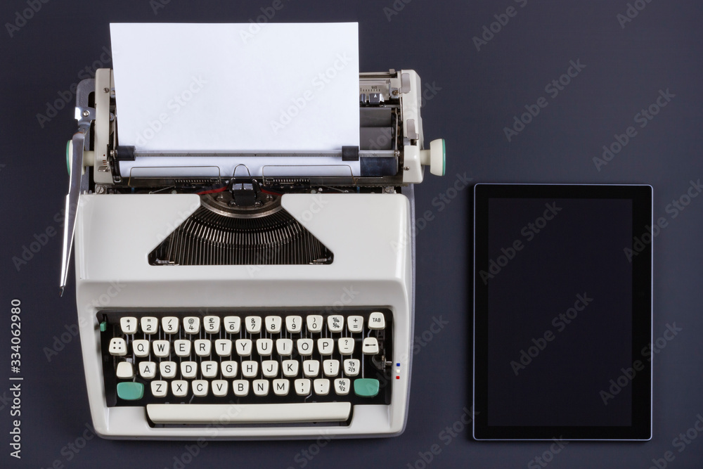 Fototapete old retro typewriter with blank paper and modern tablet on a black table. technologies of different 