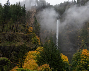 Long exposure of aMultnomah waterfalls, Oregon, USA, in the Autumn, featuring yellow colors and coniferous trees in the fog