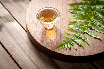 A cup of tea and a fern leaf on a walnut wooden tray.