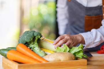 A woman chef holding and picking a fresh corn from a vegetables tray on the table