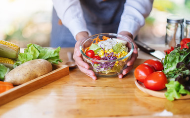 Closeup image of a female chef cooking and holding a bowl of fresh mixed vegetables salad in kitchen