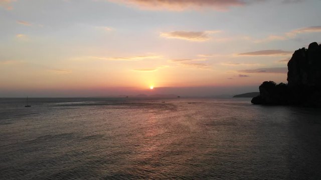 Sunrise at tropical beach at railey phra nang beach thailand drone footage. Limestone cliffs rocks in the andaman sea torquiose vacation high end resorts in sunset.