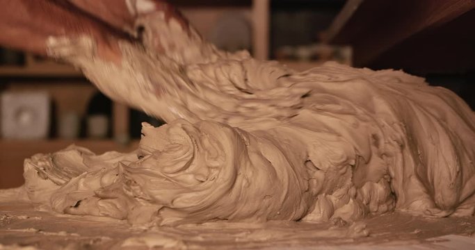 Young handsome sculptor prevents clay for making a ceramic figure. Artisan potter prepares material for his pottery. Strong male hands squeeze wet clay for modeling and sculpting. Work close-up.