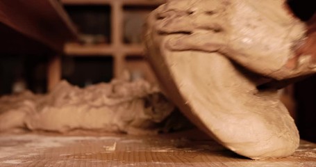 Young handsome sculptor prevents clay for making a ceramic figure. Artisan potter prepares material for his pottery. Strong male hands squeeze wet clay for modeling and sculpting. Work close-up.