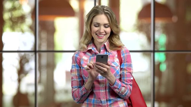 Young girl in casual cloth and purse entartaining with social media on phone. City lifestyle. Window background.