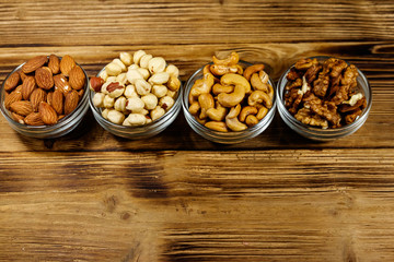 Assortment of nuts on wooden table. Almond, hazelnut, walnut and cashew in glass bowls. Healthy eating concept