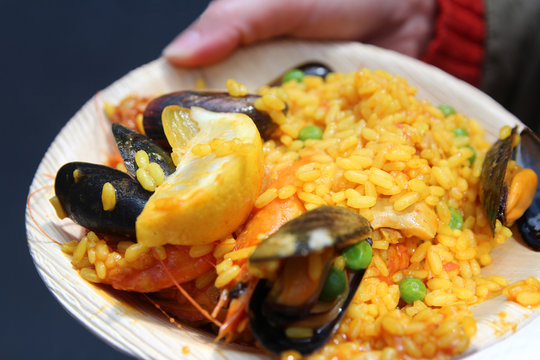 A hand holding the plate of seafood Paella in a plate at Borough Market, London, UK