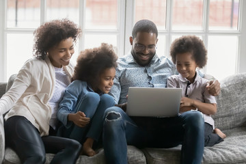 African couple and kids look at pc screen engaged at search of best offer travel full family trip, booking hotels use websites services buy on-line, make videocall, surfing web, watch cartoons concept