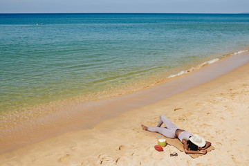 Female jogger resting on beach after running and covering face from the sun with straw hat
