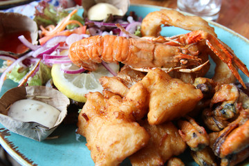 Mixed fried seafood such as shrimp, calamari, fish and mussel with salad, tartar sauce and mayonnaise on a plate
