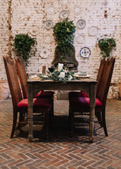 Fototapeta na wymiar A table and a table setting designed for an intimate boho style event with rustic touches complemented with red velvet chairs