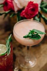 A creamy alcoholic cocktail garnished with mint in a rustic setting with white and pink florals in the background