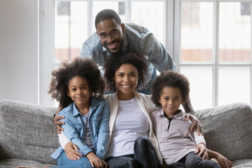 Mixed race African ethnicity full family gathered together in living room photo shooting look at...