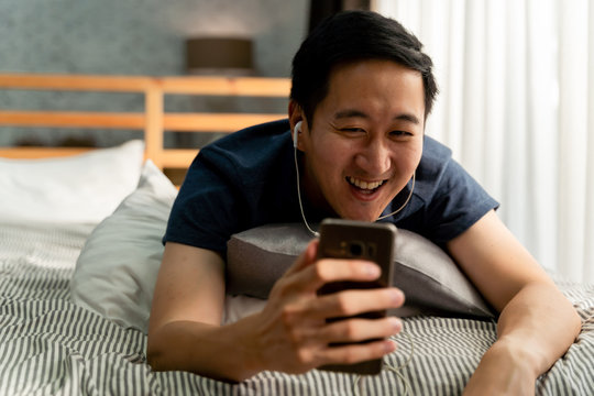 Portrait Of Happy 30s Aged Asian Man In Casual Clothing Making Facetime Video Calling With Smartphone At Home. Using Conferencing Meeting Online App, Social Distancing, Work From Home Concept