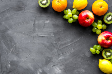 Fresh fruits background with citruses, apple, kiwi and grape on grey table top-down frame copy space