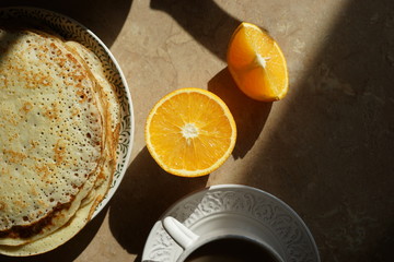 Pancakes and oranges on the table in the kitchen on a sunny day