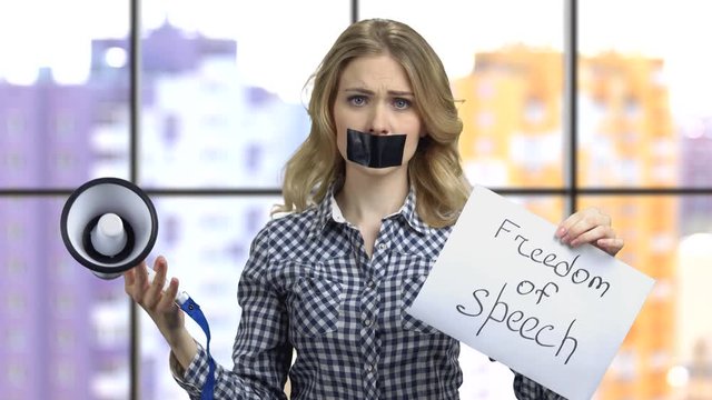 Freedom of speech concept. Young girl with black tape over mouth trying to speak in megaphone.